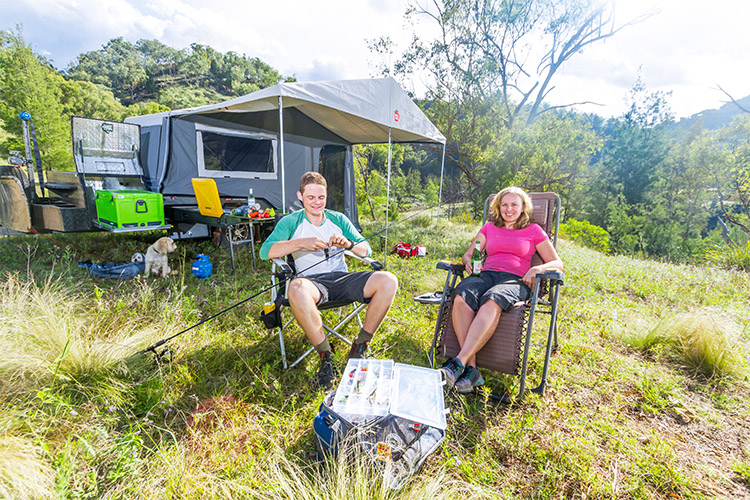 Two people sitting on chairs in front of their camper trailer