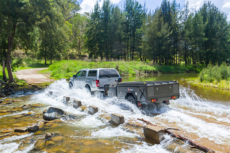 Car and camper trailer driving through a river