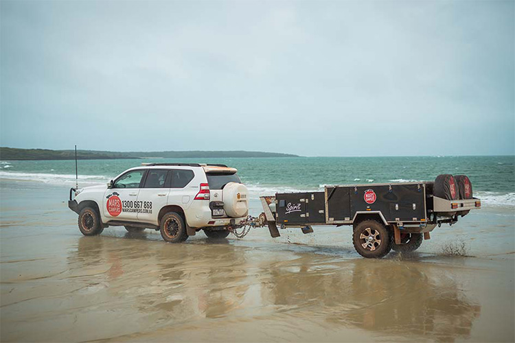 Car and camper trailer driving on a beach