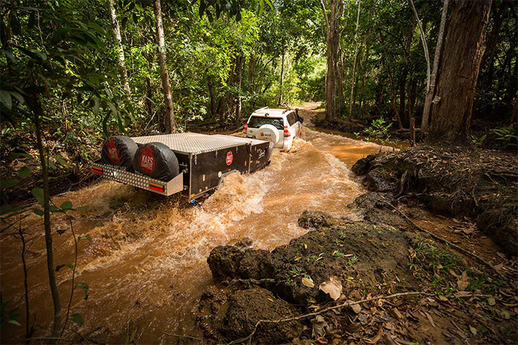 Car and camper trailer driving through a muddy river