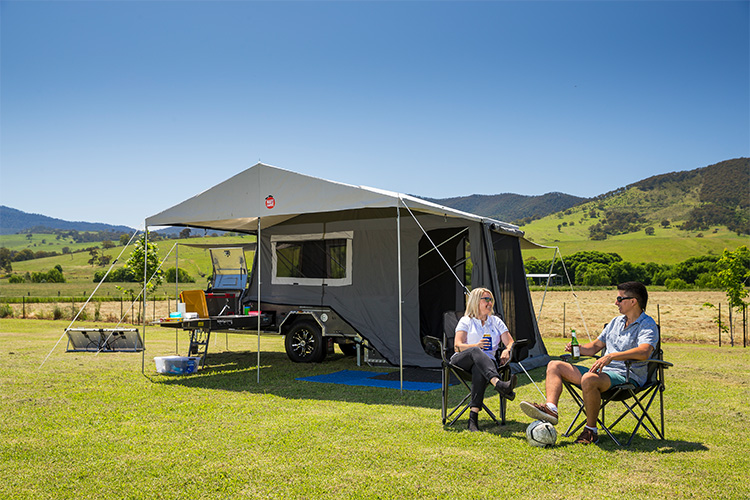 Two people sitting on chairs in front of a camper trailer