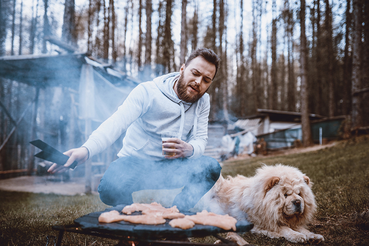 Hipster Male On Camping With His Dog Making Barbeque