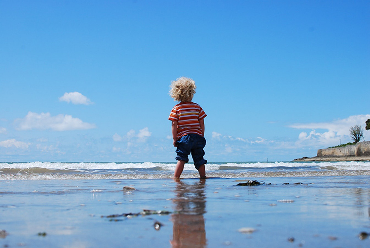 Kid looking at blue sky from beach